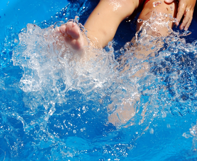 Detail of a child's feet kicking water in a swimming pool