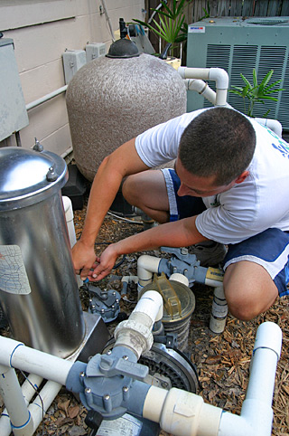 a service man kneels between the pipes of a pool pump